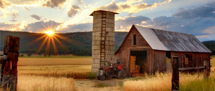 Barn in autumn field with old tractor parked in front as the sun sets behind the ridge in the background.